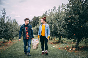 一男一女拿着一袋营养苹果走过苹果园。