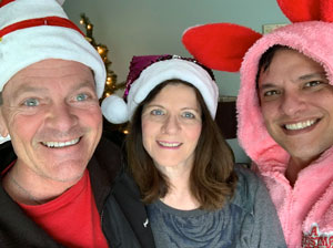 一对50多岁的夫妻和30多岁的儿子，戴着圣诞老人的帽子，对着镜头微笑。
